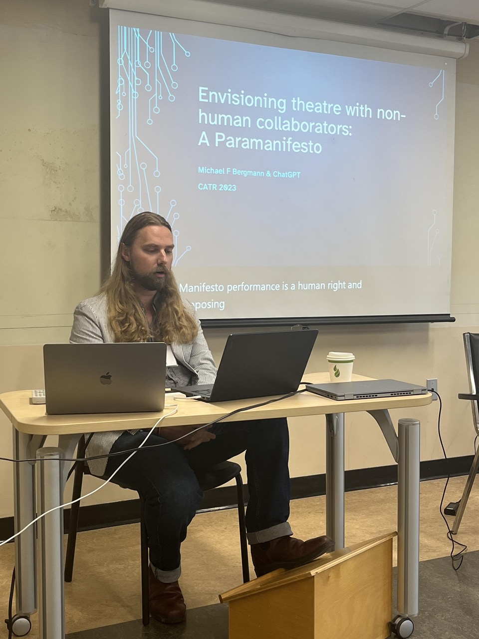 Michael presents at the conference, his presentation is projected behind him title reads "Envisioning theatre with non human collaborators: a paramanifesto" 